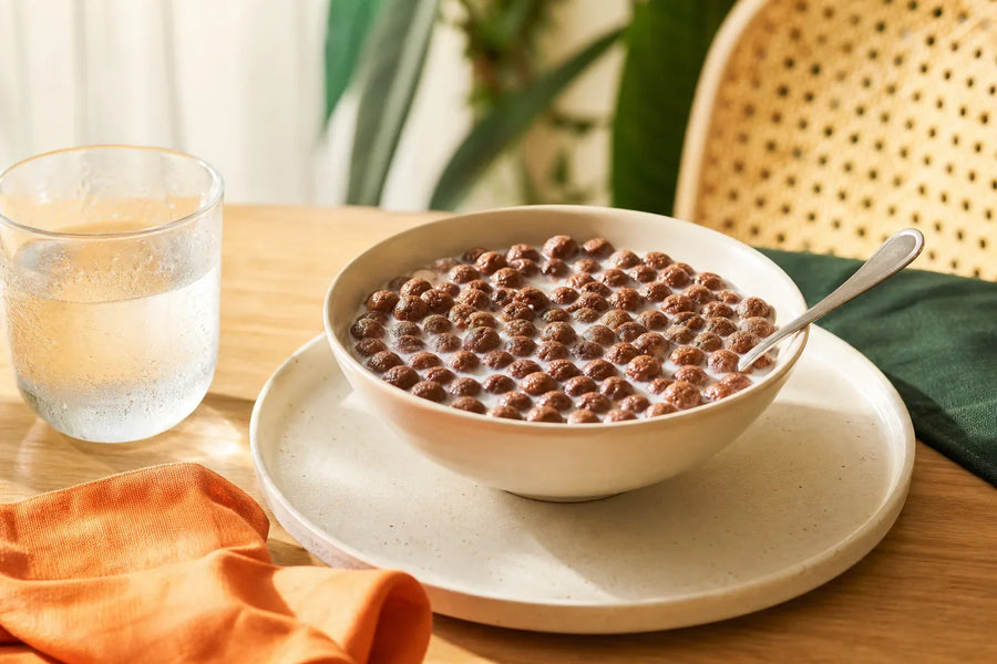 Tigela de cereal de cacau com leite gelado e copo com condensação.