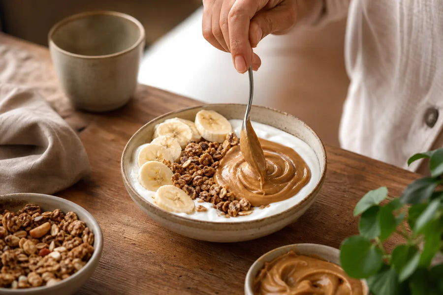 Pessoa finalizando bowl de iogurte, banana, granola e pasta de amendoim.