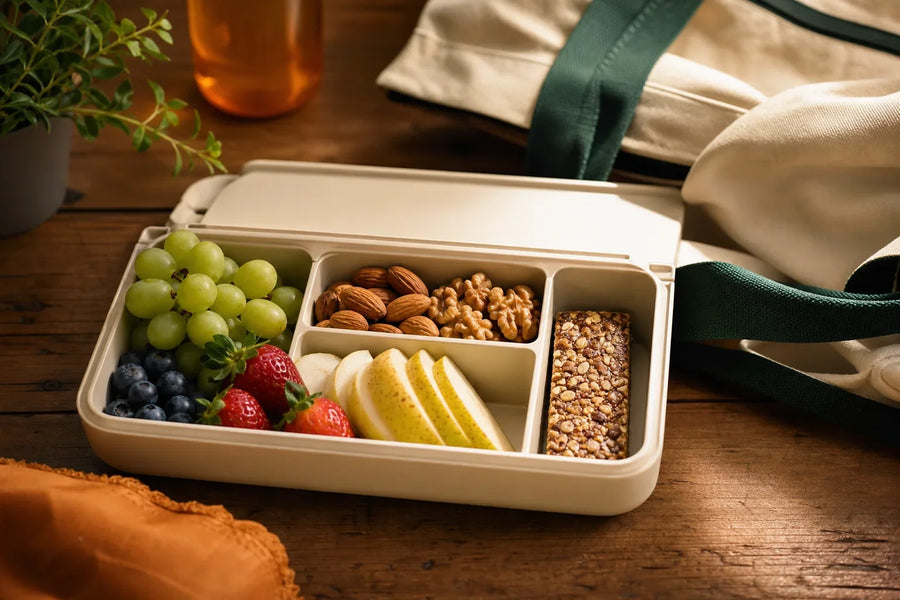 Lancheira aberta com uvas, frutas vermelhas, pera, castanhas e barra.