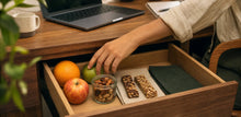 Gaveta de trabalho aberta com frutas, castanhas e snacks.