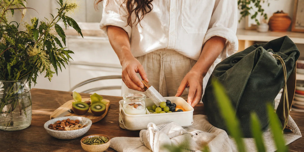 Pessoa montando uma lancheira com frutas, iogurte, castanhas e snack